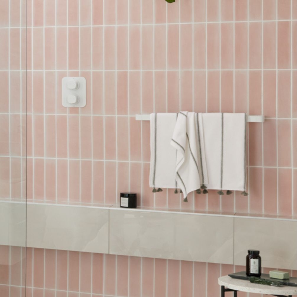 product lifestyle image of vado cameo 600mm matt white towel rail and shelf hanging towels in peach salmon pink bathroom with brick vertical tiles mus-184-60-mw